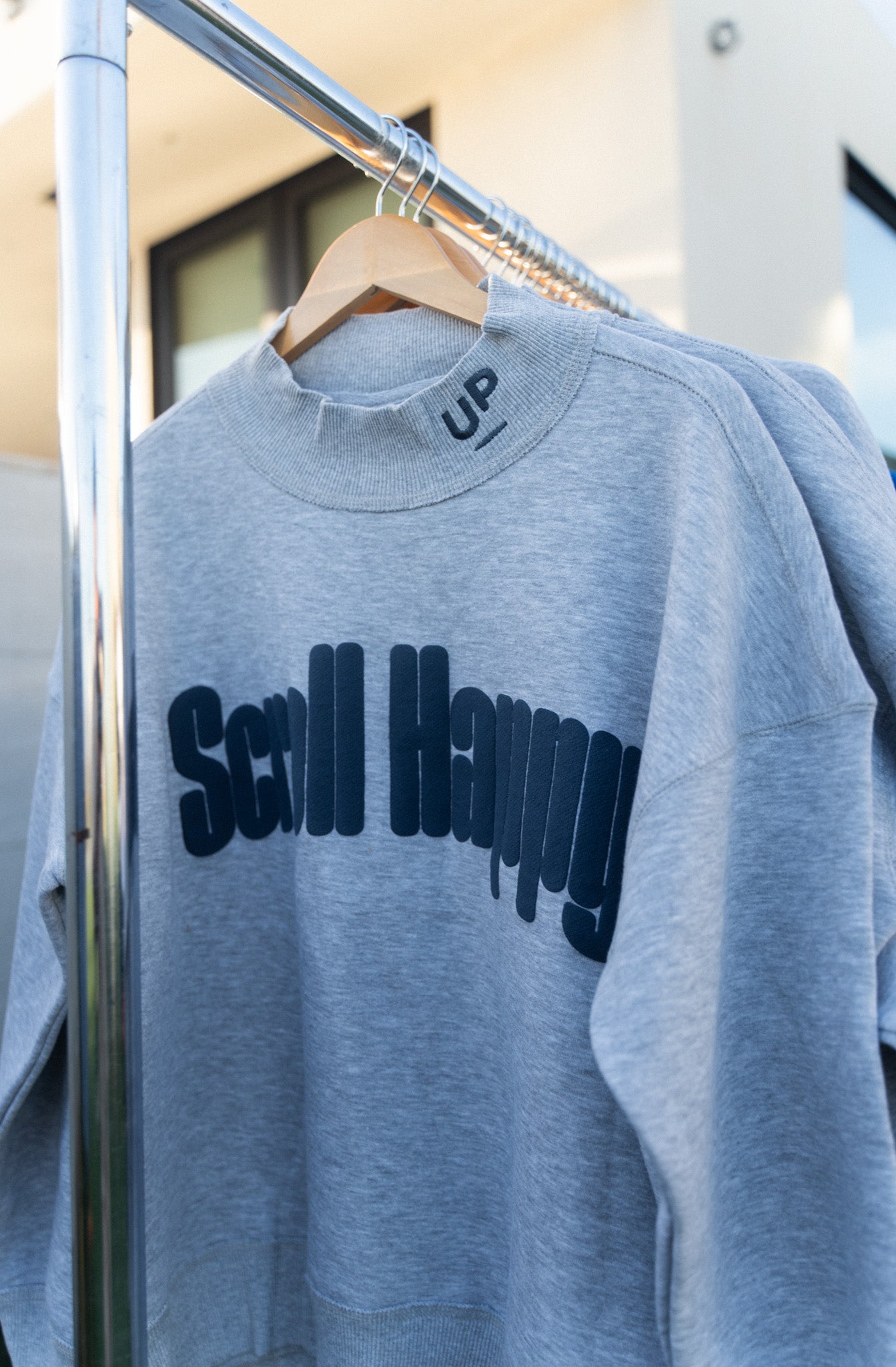 Grey Scroll Happy mock neck sweatshirt on a hanger, navy wordmark across the chest