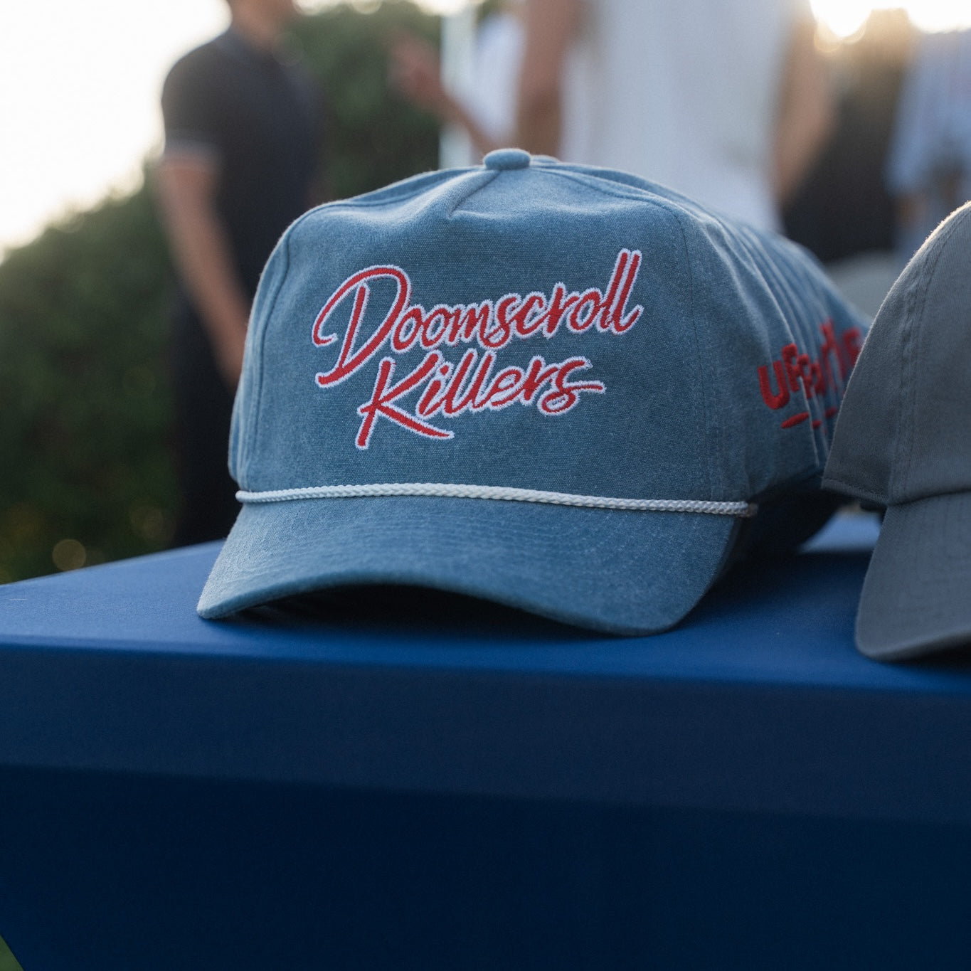 Denim blue Doomscroll Killers rope cap on a table at an outdoor event
