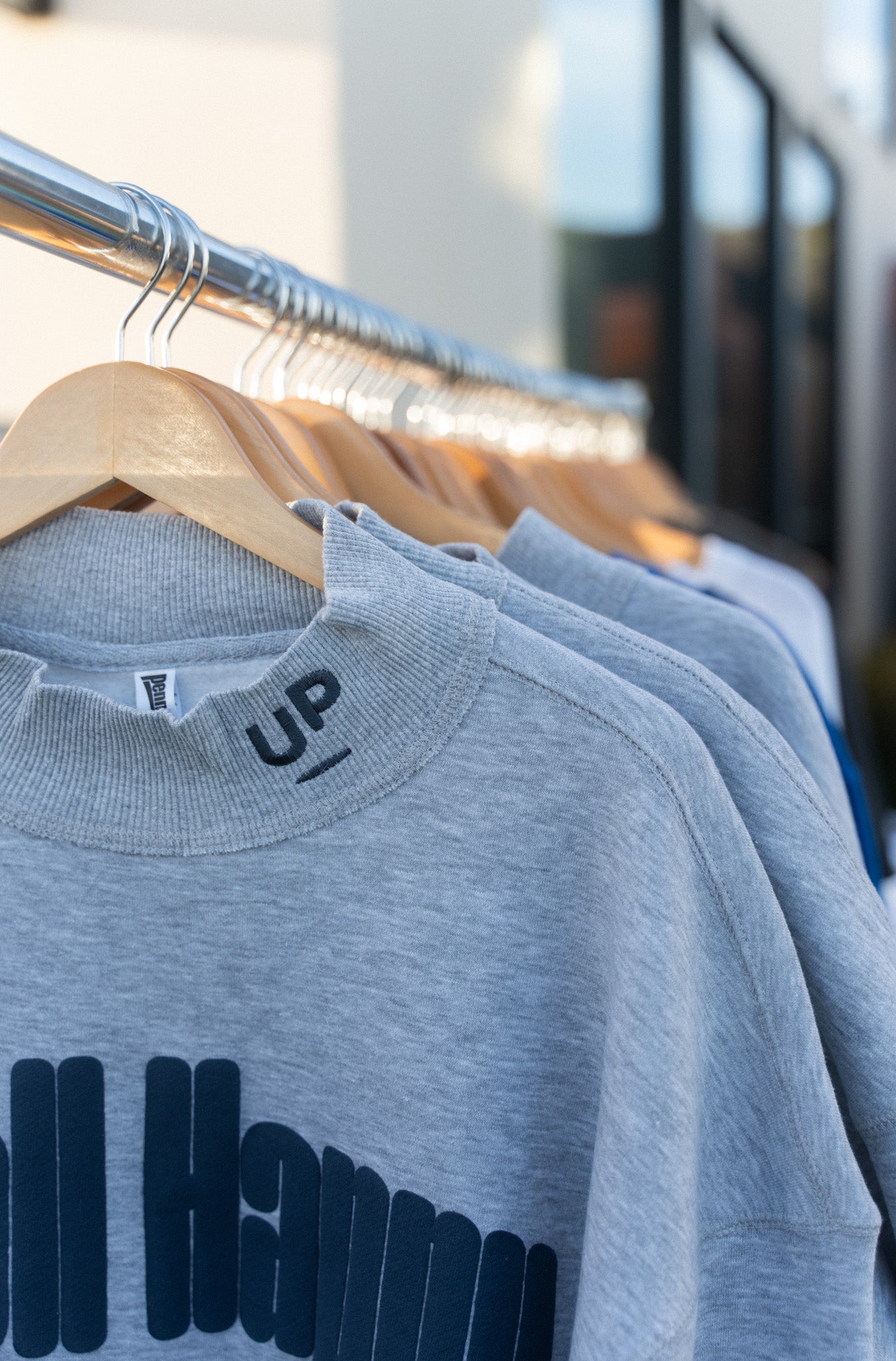 Close-up of the embroidered UP logo at the mock neck collar of the grey sweatshirt