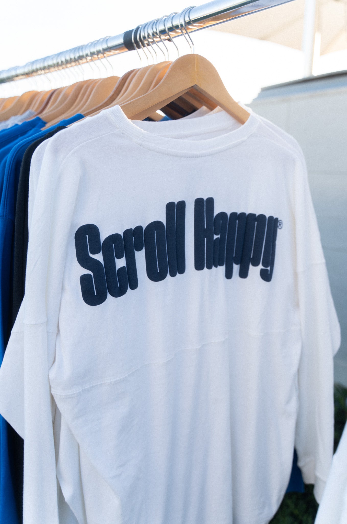 White Scroll Happy long sleeve shirt on a rack, navy wordmark across the back
