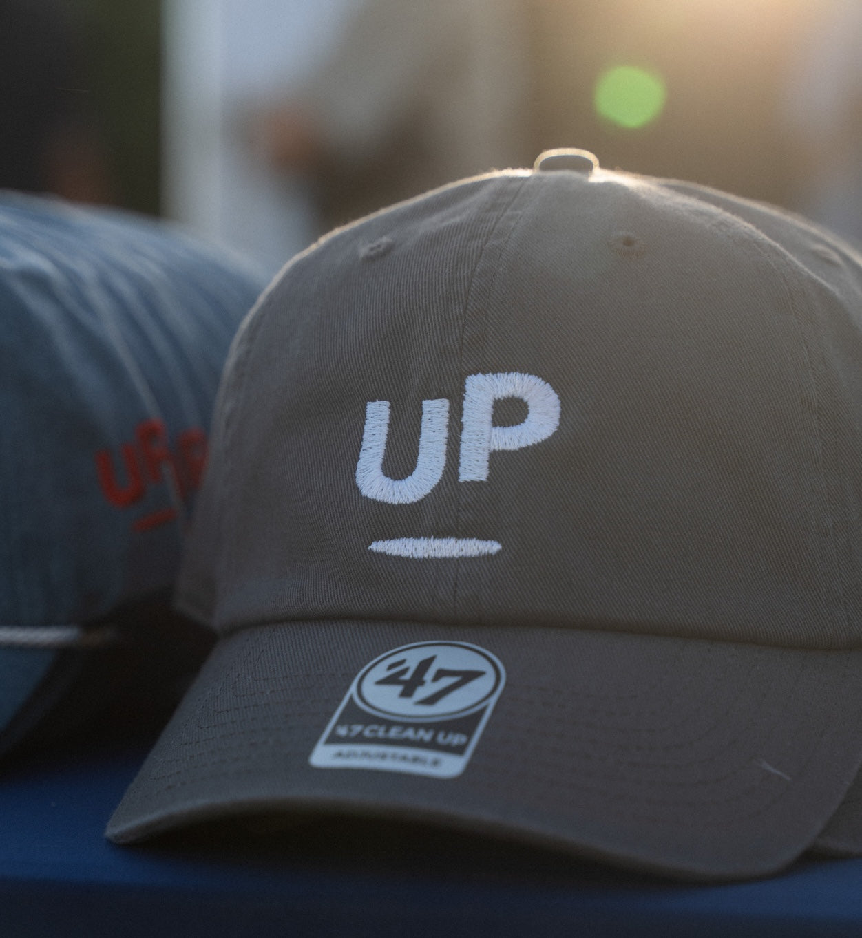 Grey UP dad hat with the white UP logo on a table at an outdoor event