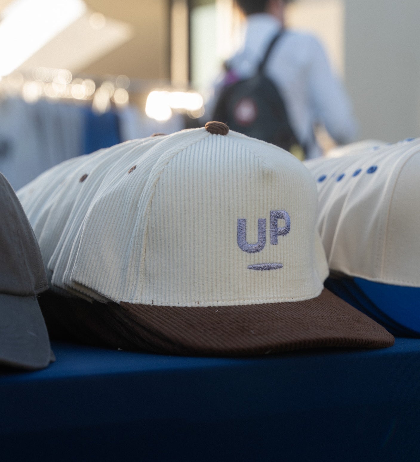 Cream and brown corduroy UP caps on a table at an outdoor Scroll Happy event