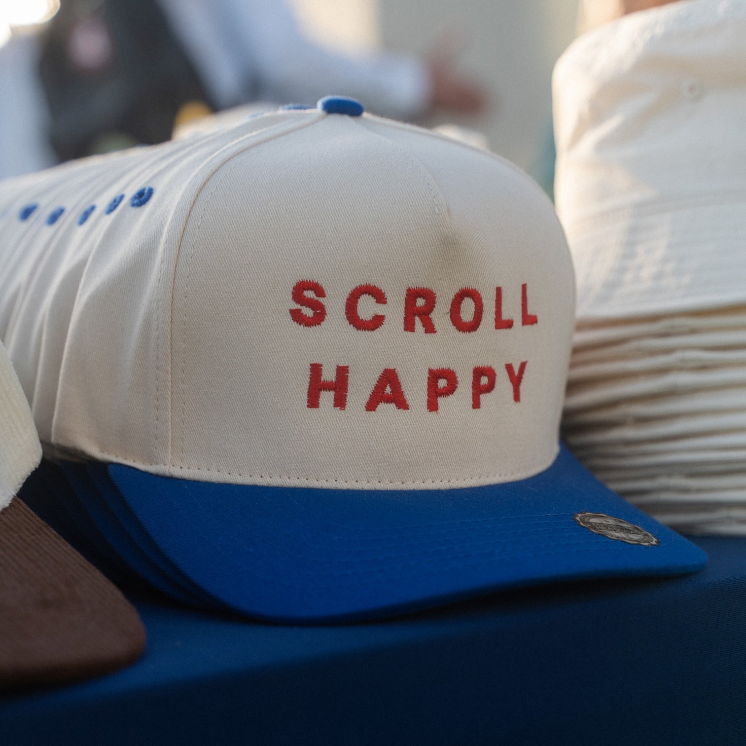 Cream and blue Scroll Happy caps with red embroidery on a table at an outdoor event