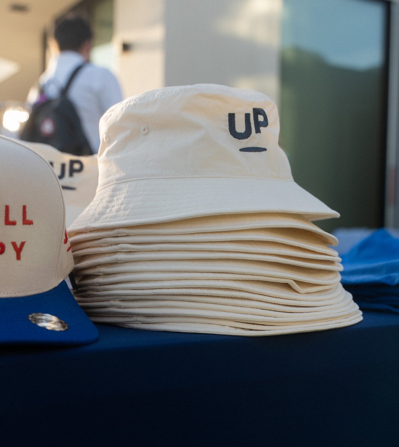 Stack of cream UP bucket hats at an outdoor Scroll Happy event